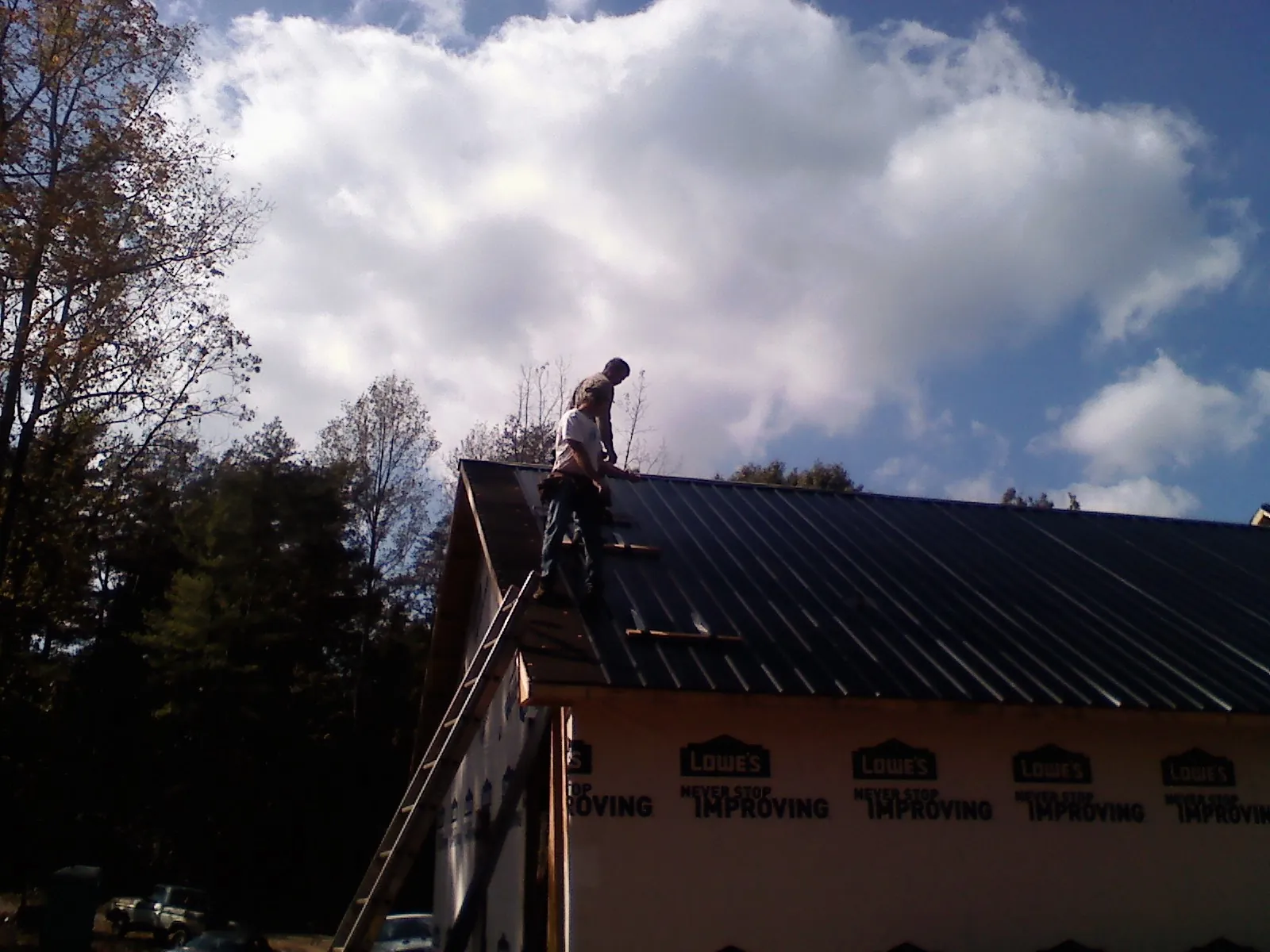 Roofer fastening dark metal panels high against a cloudy sky, from a Roof Inspection job in Riverside