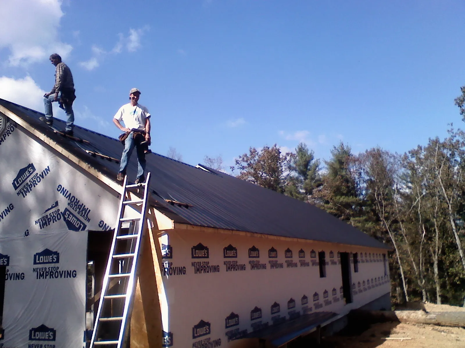 Two roofers standing on a long dark metal roof over a wrapped building in Riverside